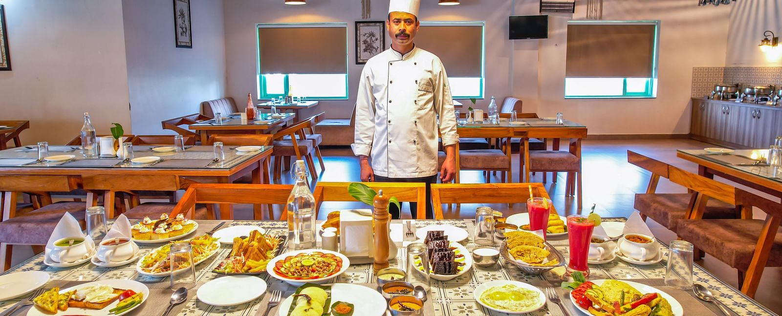 A chef stands near tables laden with food in a dining area at Vedikant Resorts The Mallard Corbett.
