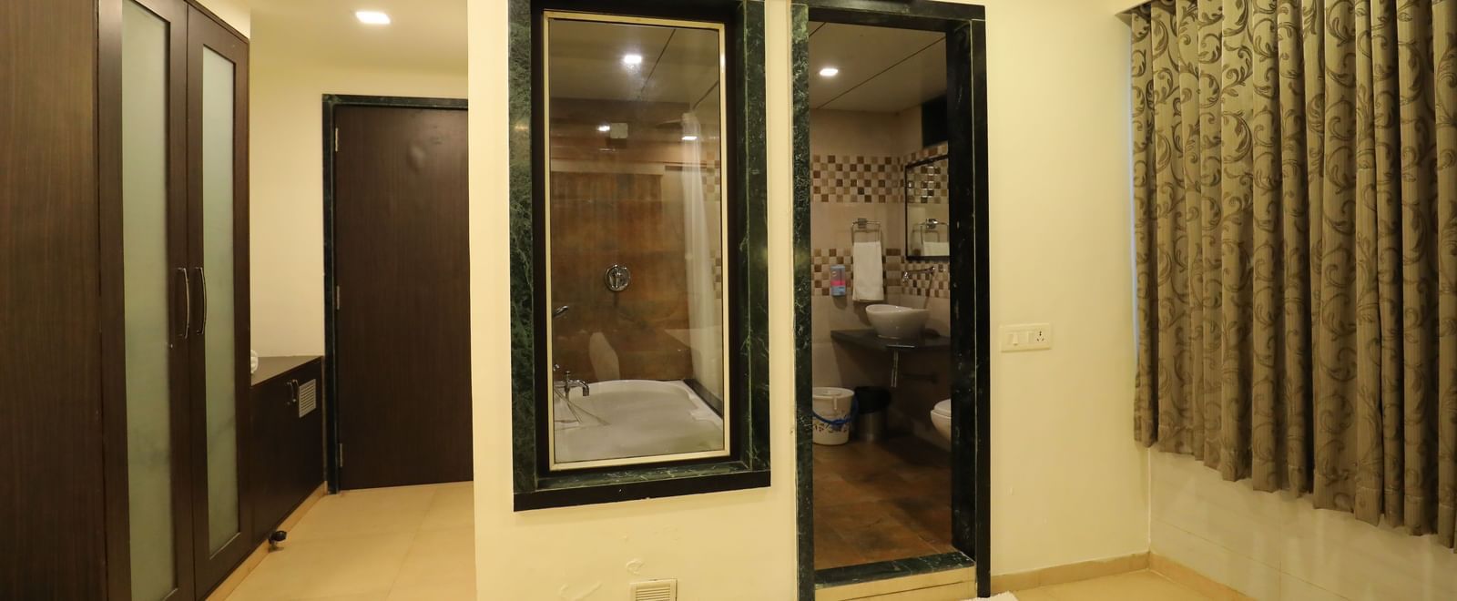 The entrance area to a Krushnai Resort room, showing a wardrobe and a glass panelled wall with a view of the washroom.