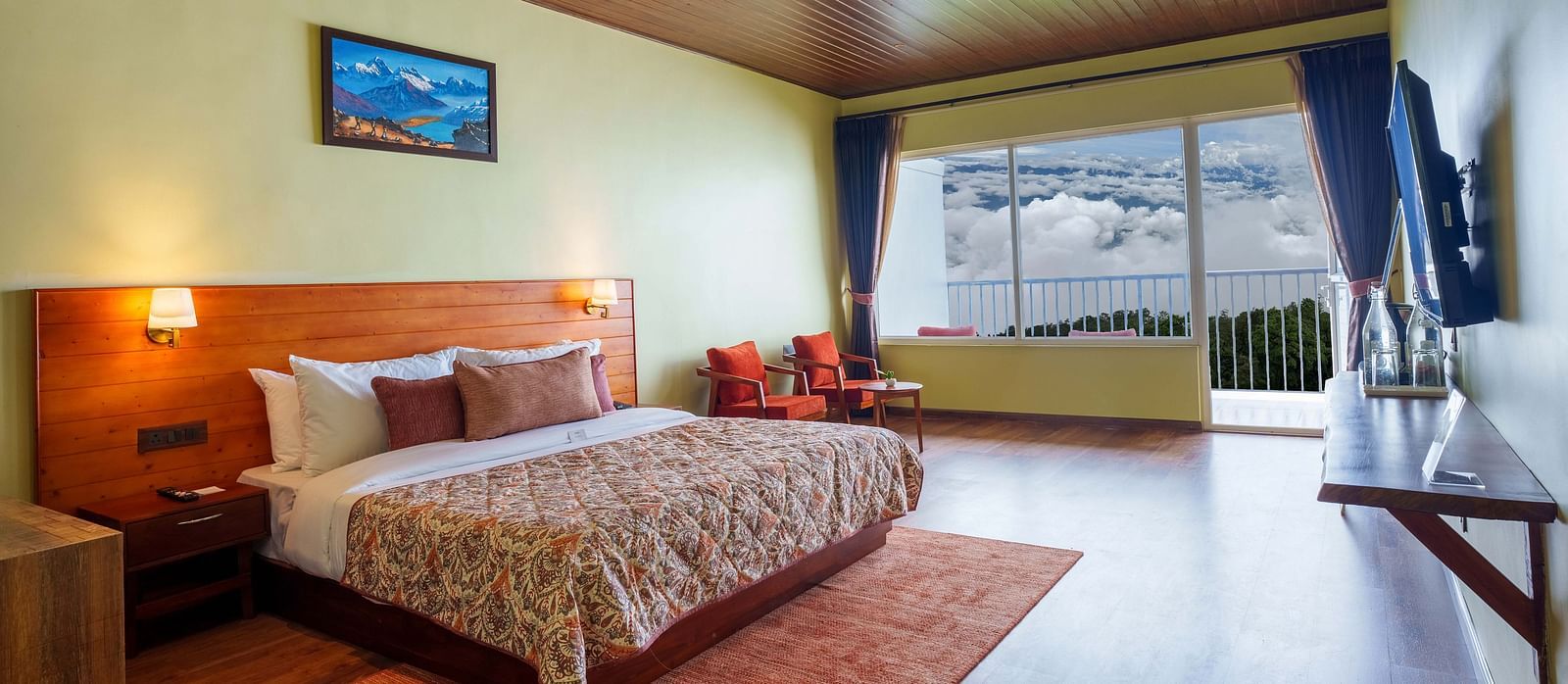 A tastefully decorated hotel room at Summit Enigma Resort & Spa, Lamahatta, with a large bed, a television, and a balcony offering an outdoor vista.