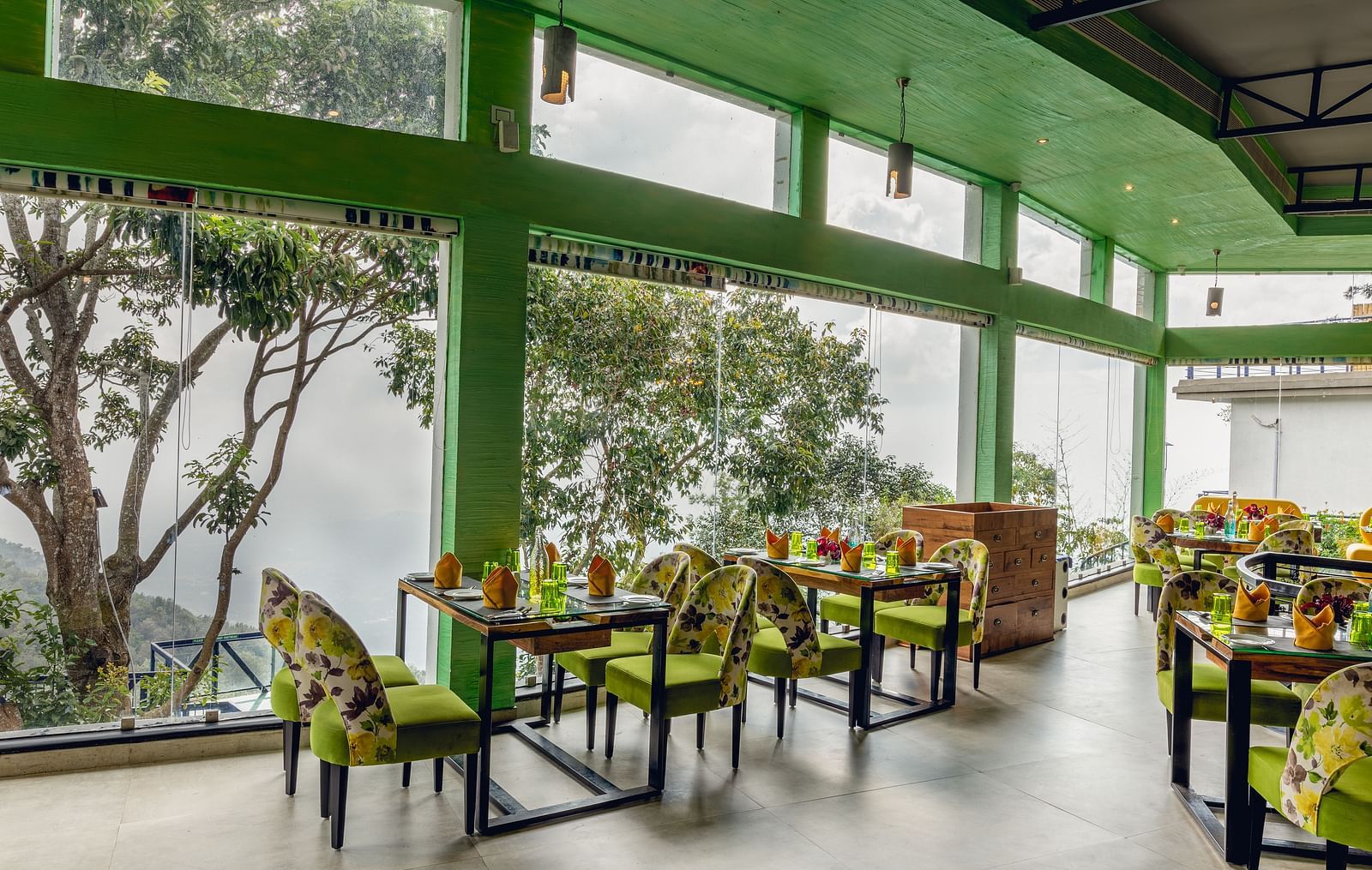 An image of a restaurant with seating arrangement and expansive glass window over looking the serene mountains - Great Trails Yercaud by GRT Hotels