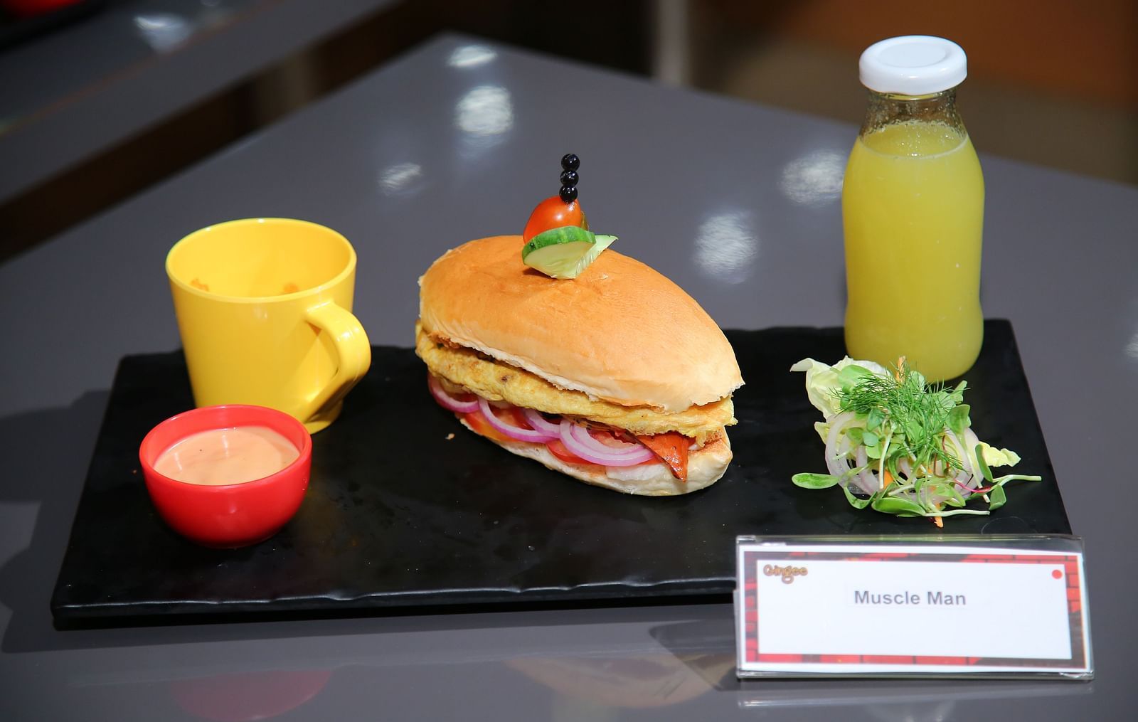 A breakfast platter featuring a toasted sandwich filled with scrambled eggs and vegetables, a side salad, a cup of soup, a bottle of juice, and dipping sauce.