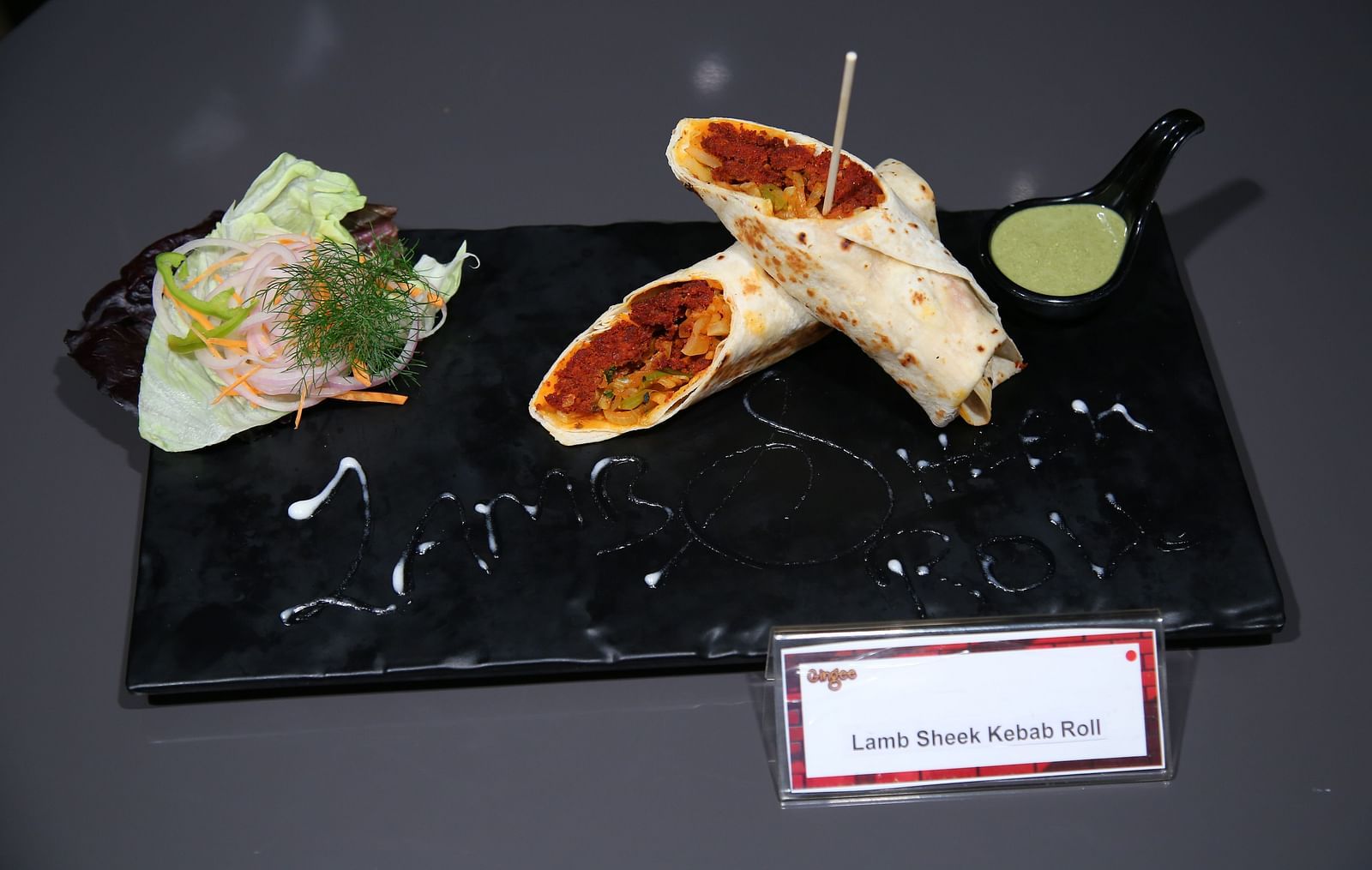  Two rolled wraps with a red filling on a black plate, accompanied by a green sauce and a side salad.