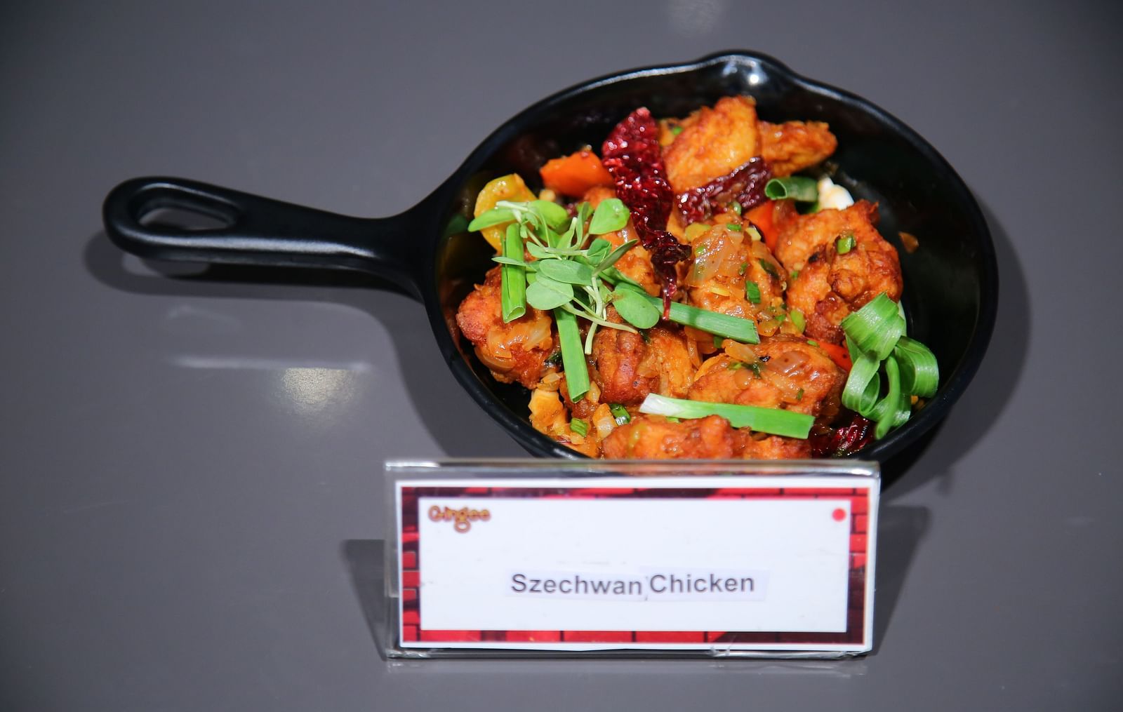 A black cast iron skillet filled with Szechwan chicken, garnished with green onions and red peppers.