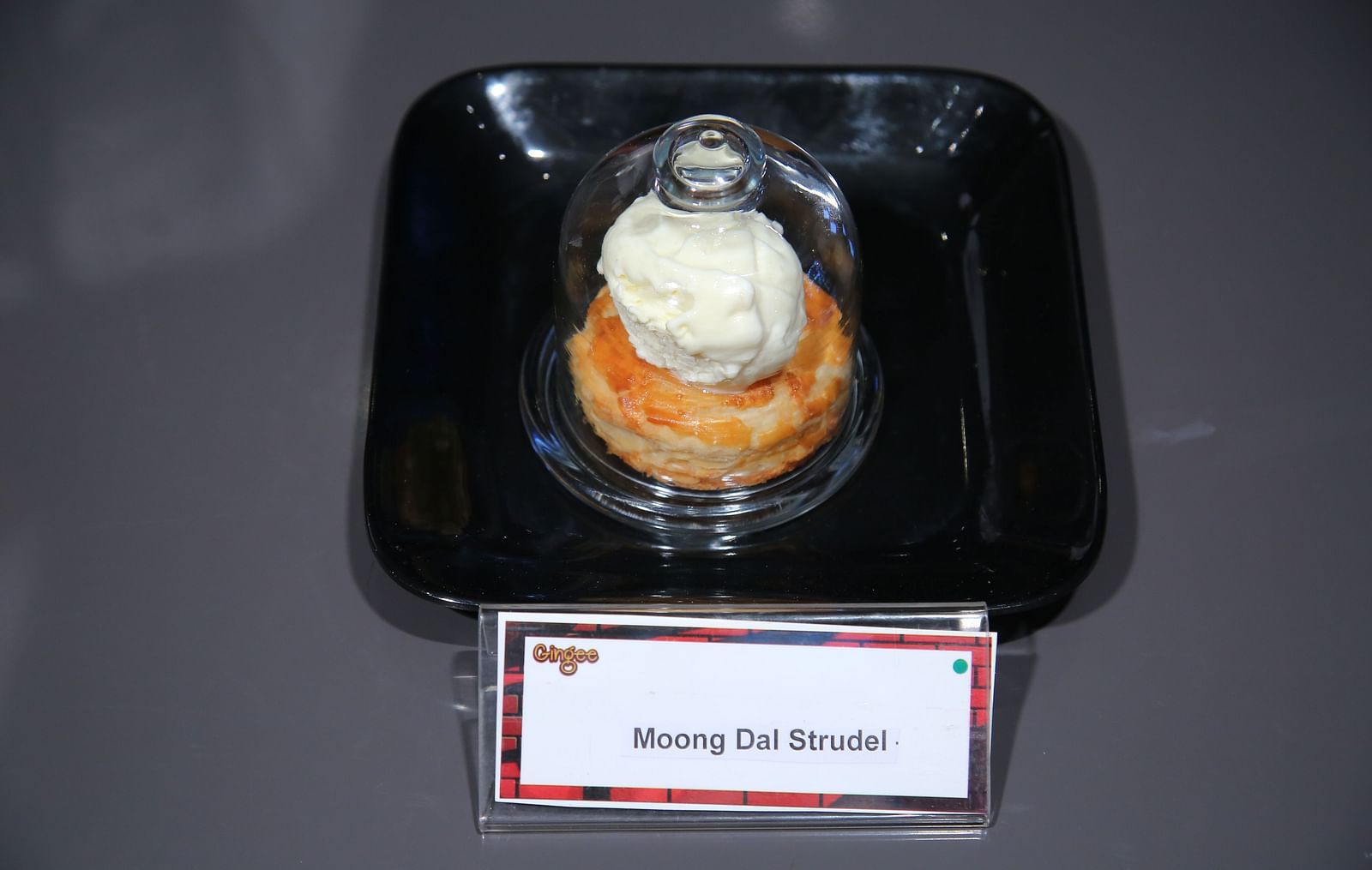 A pastry topped with a scoop of vanilla ice cream, served on a black square plate.