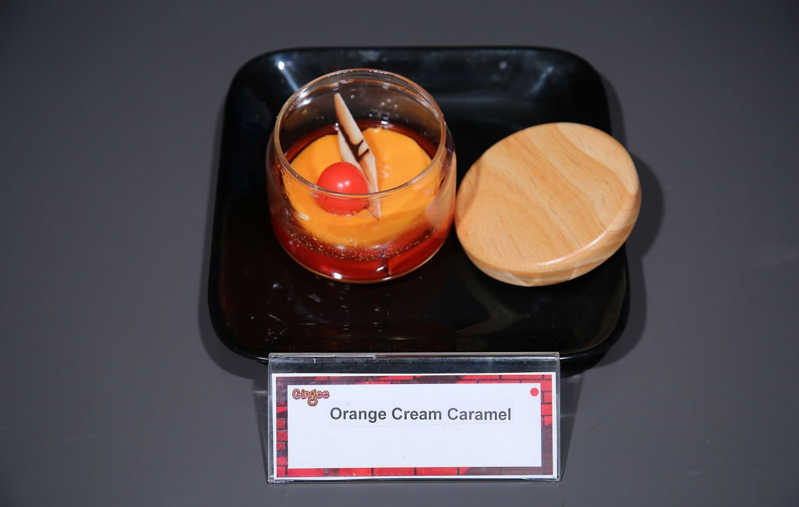 A glass jar filled with an orange-colored drink, garnished with a maraschino cherry and a cinnamon stick