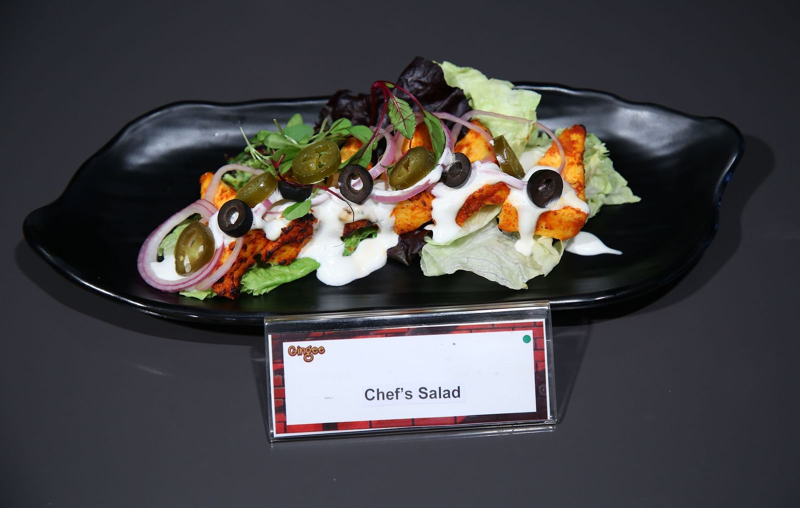 Chargrilled salad with grilled chicken, mixed greens, vegetables, and a creamy dressing, served on a black plate.