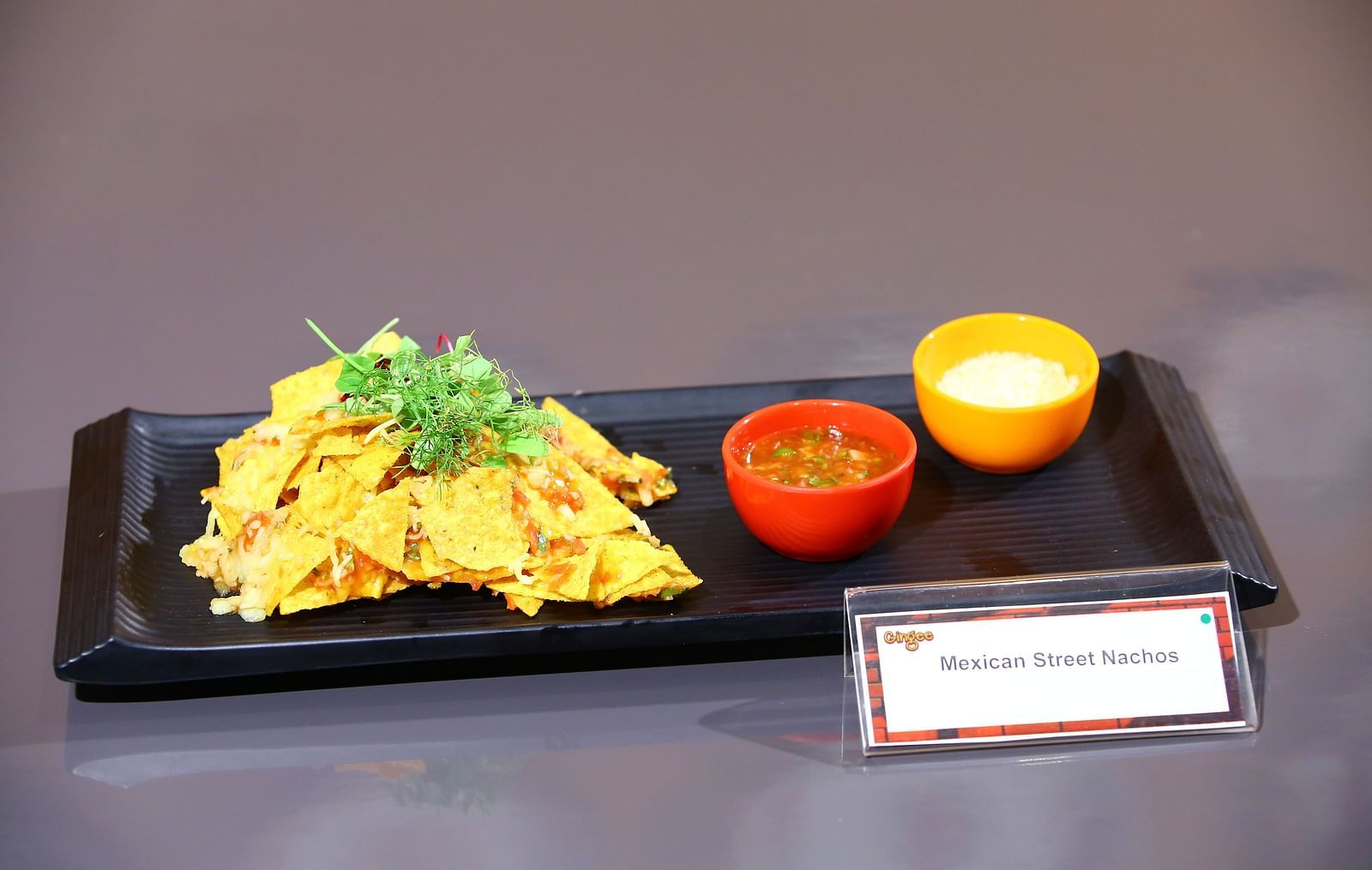 Crispy nachos loaded with toppings and served with red and yellow dipping sauces.