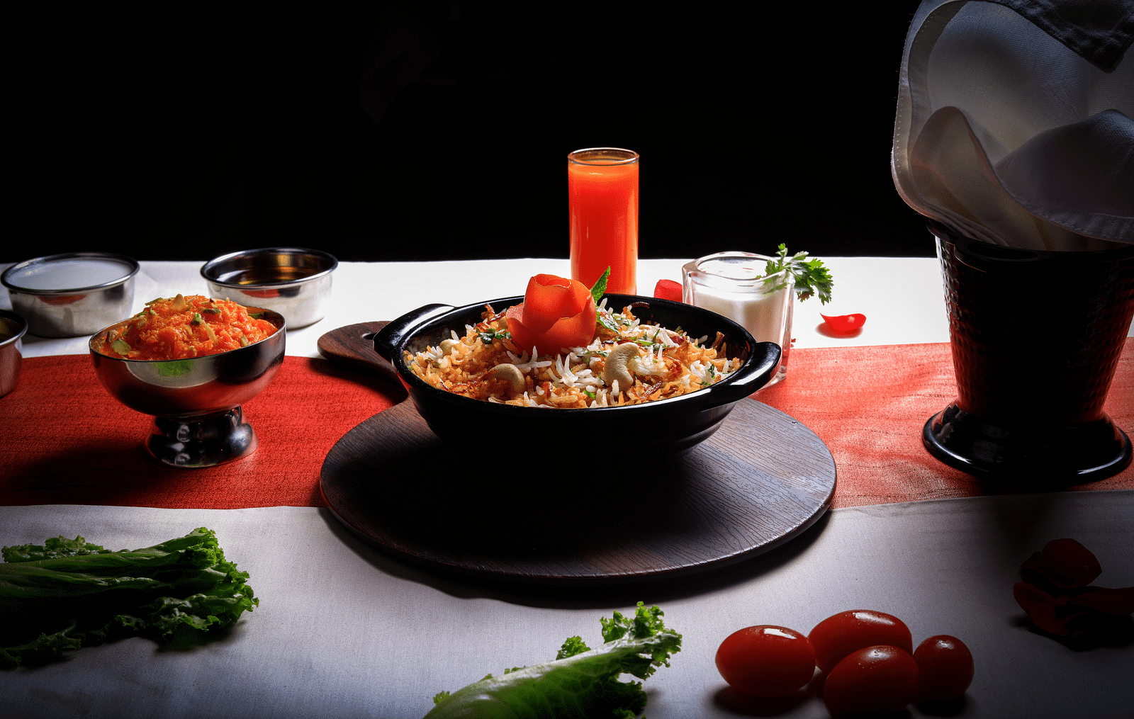  A bowl of creamy, orange-hued pasta topped with a dollop of red sauce and a sprig of parsley. The dish is accompanied by a glass of orange juice, a chef's hat, and various vegetables.