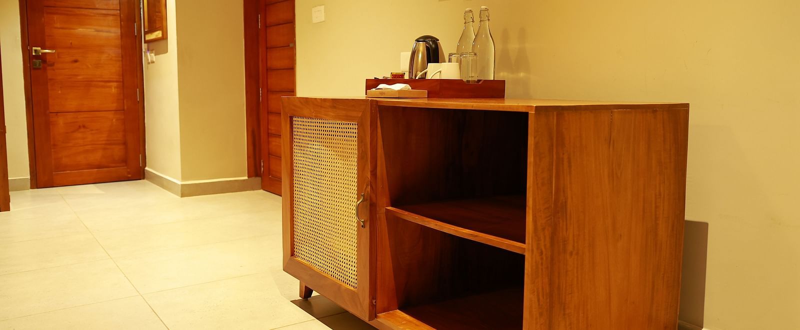  A functional wooden cabinet with a kettle and glasses in a room at Vaasta Vagamon, with two wooden doors in the background.