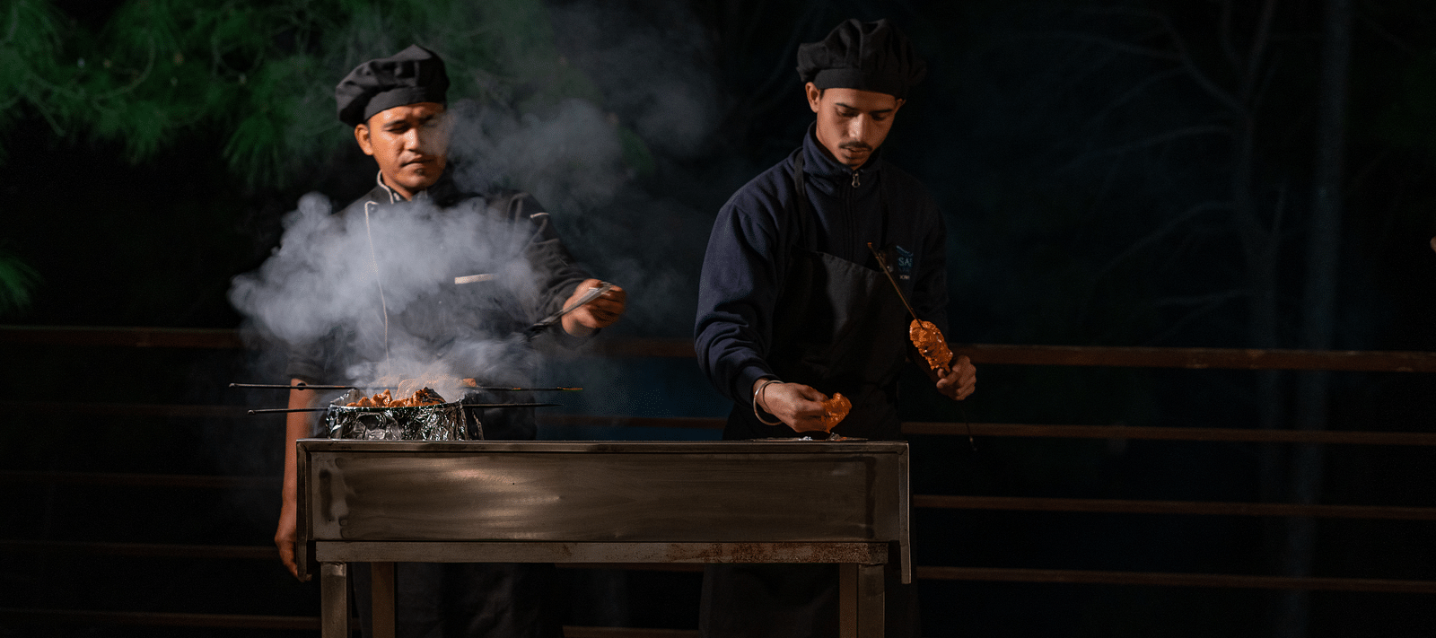 Two chefs preparing barbecues with smoke rising from the sizzling grills at BluSalzz Escapade Resort, Lansdowne