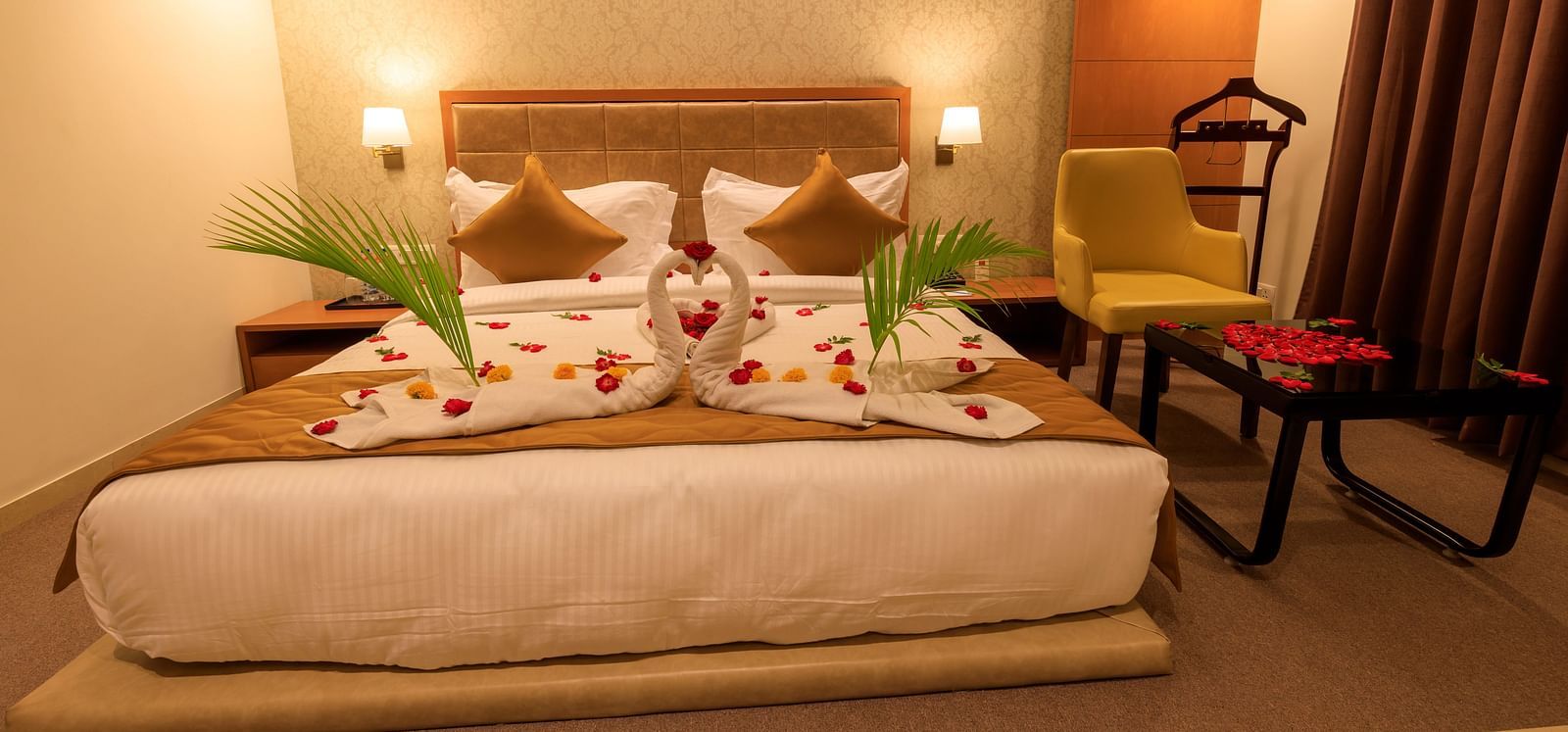 A warmly lit hotel room at Lords Eco Inn Apple Gate features a decorated double bed, bedside tables, a chair, and brown curtains.