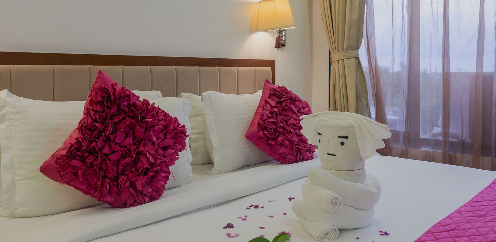Hotel room bed at Diamond Palace Lords Plaza with decorative pillows, towel art, and rose petals.