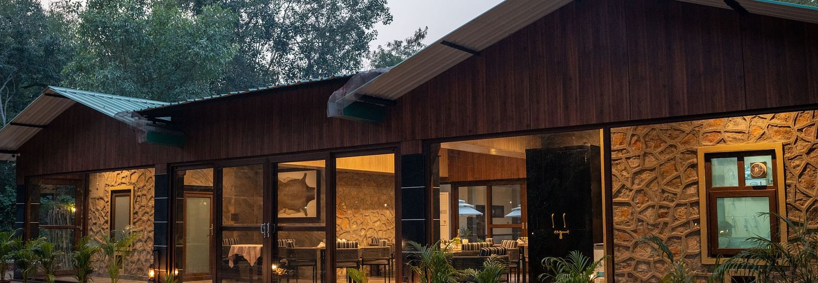 The inviting exterior of Aamaghati Jungle Retreat Ranthambore lit up in the evening amongst the trees.