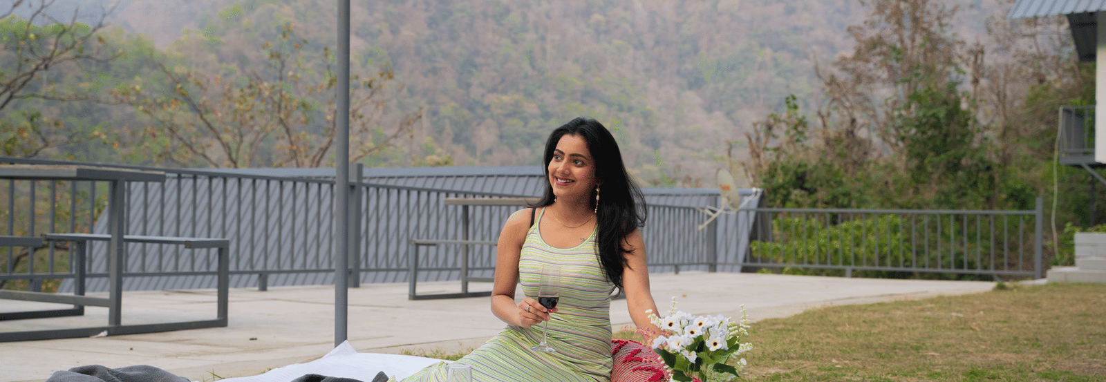 A person sits on a picnic blanket on the grass at Perfect Stayz The Jungle Resort, surrounded by food and flowers.