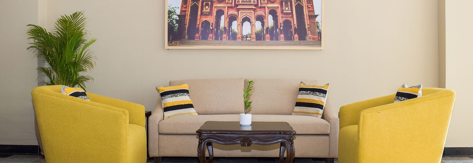A hotel lobby seating area with yellow armchairs, a beige sofa, a dark wood coffee table, a framed image of a building, and a potted plant - Urban Suites by BluSalzz, Jaipur
