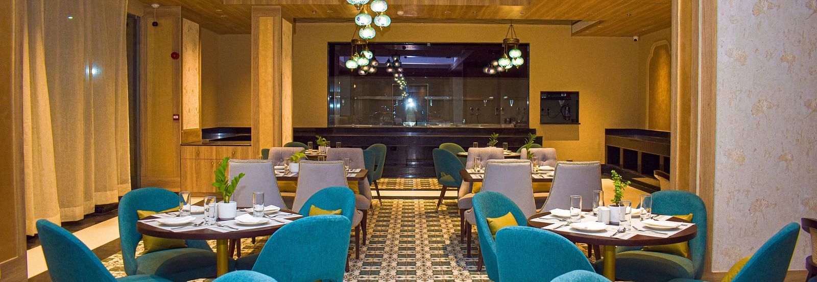 A modern restaurant interior with teal armchairs, round tables, patterned tile floor, and a distinctive globe chandelier - Urban Suites by BluSalzz, Jaipur