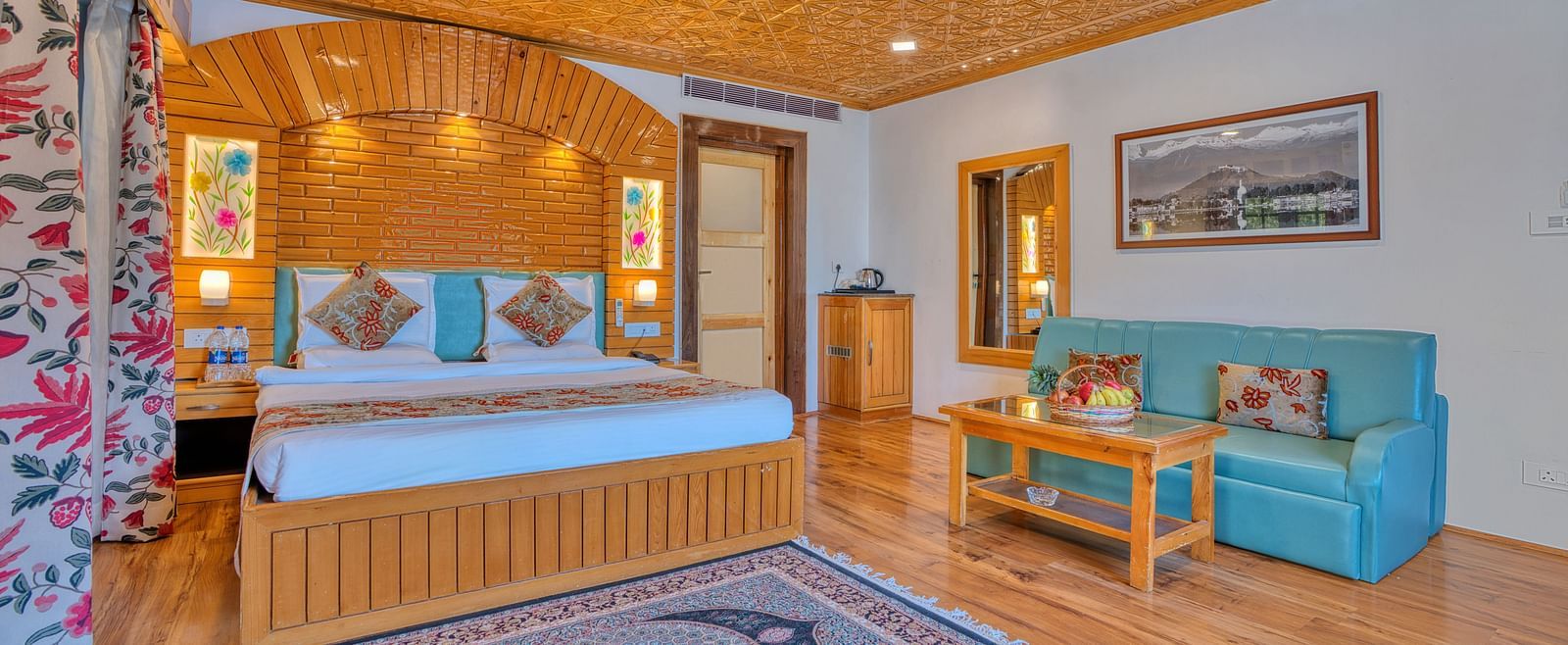 Cosy suite with wooden bed frame, teal sofa and warm lighting at Royal Comfort Regency, suited for both leisure and business stays.