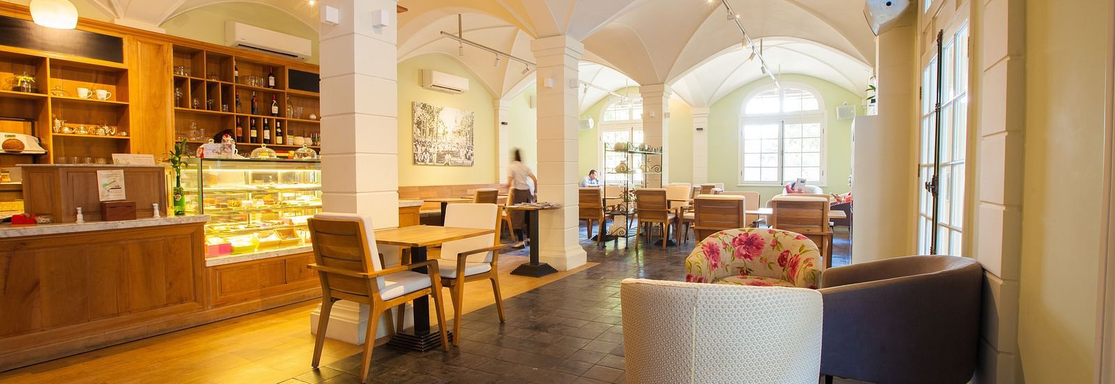 A cafe with tables and chairs, and a long counter with display shelves | The Shop | Central Mansions, Phnom Penh