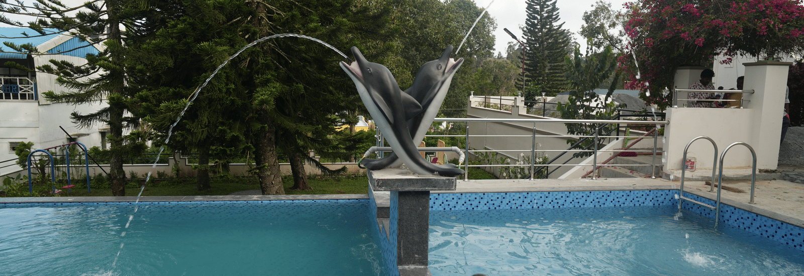 The swimming pool at WOW Naturefull Resorts with 2 dolphin statues in the middle of it.