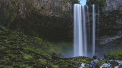 a person sitting on a boulder looking at a waterfall in the distance