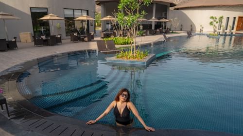 A woman relaxing at the edge of a modern outdoor swimming pool, surrounded by loungers and property at Ananta Spa and Resort, Ajabgarh.