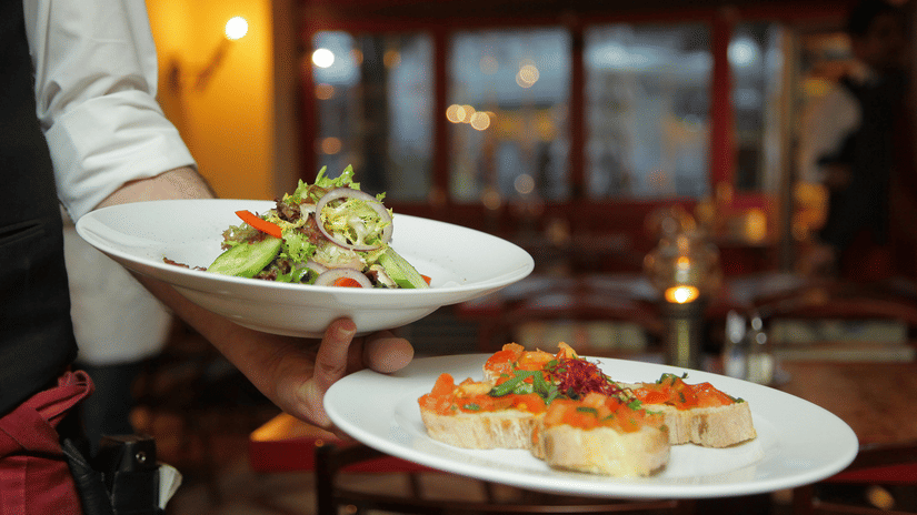 A person in a restaurant holding two plates with delicious cuisines in it that are well plated