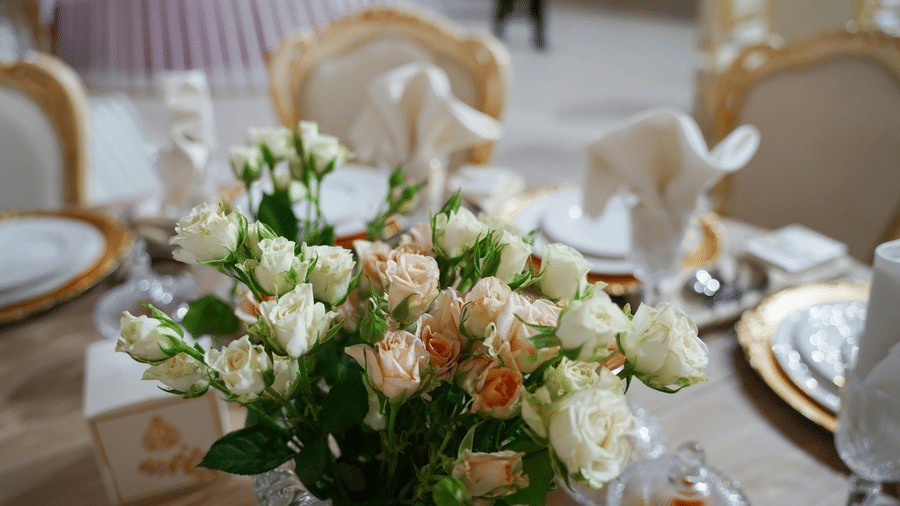 A close up shot of a beautiful flower vase with a lot of white and pink roses on a dining table.