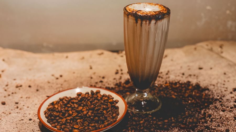 An image of a glass of coffee and near it coffee beans are scattered in and outside a late - The Garden Ananta Elite, Rajkot 