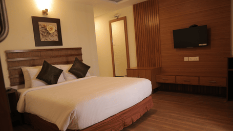 Family friendly room with a double bed, wooden headboard and wall mounted television in warm lighting at Benzz Park, Kodaikanal.