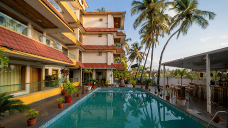 An outdoor swimming pool with surrounding building structures, palm trees, seating area, and a pool at Perfectstayz Premium Goa Continental Baga, Arpora..