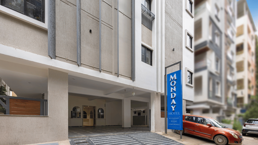 A multi-storey building exterior displaying a blue sign for Monday Hotels & Suites Madhapur Hyderabad near a covered entrance driveway.