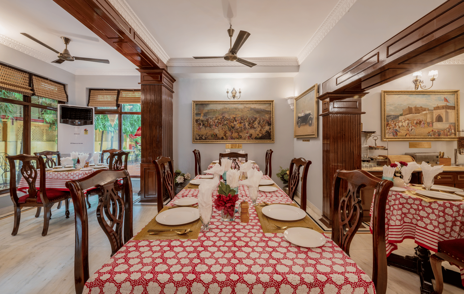 Traditional dining hall with red checkered tablecloths, wooden pillars, and chandelier at Dera Rawatsar, Jaipur.