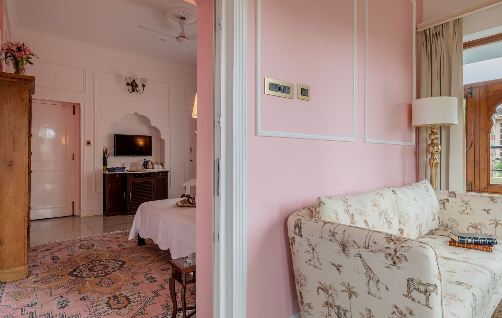 Guest room with pink walls, patterned flooring, seating area, and wooden furniture at Dera Rawatsar, Jaipur.
