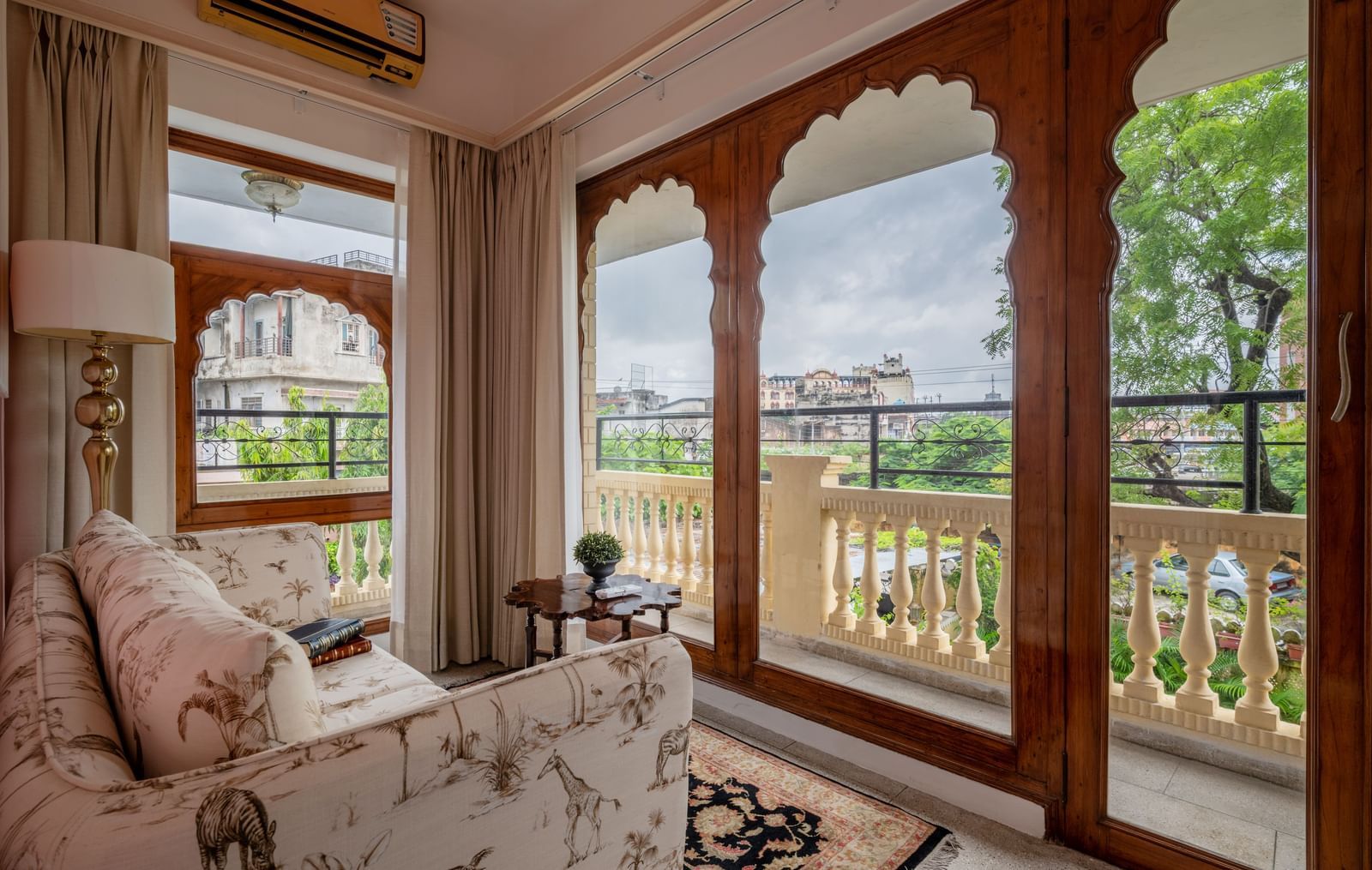 Sitting room with upholstered furniture, large arched windows, and views of greenery at Dera Rawatsar, Jaipur.