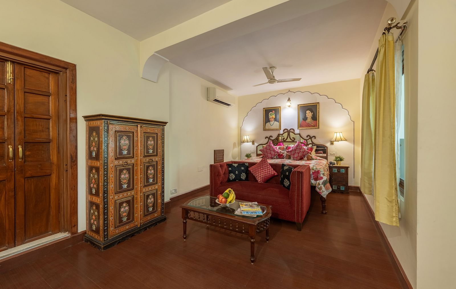 A bedroom with a red sofa, decorative wardrobe, wooden doors, and arched architectural details | Dera Rawatsar, Jaipur