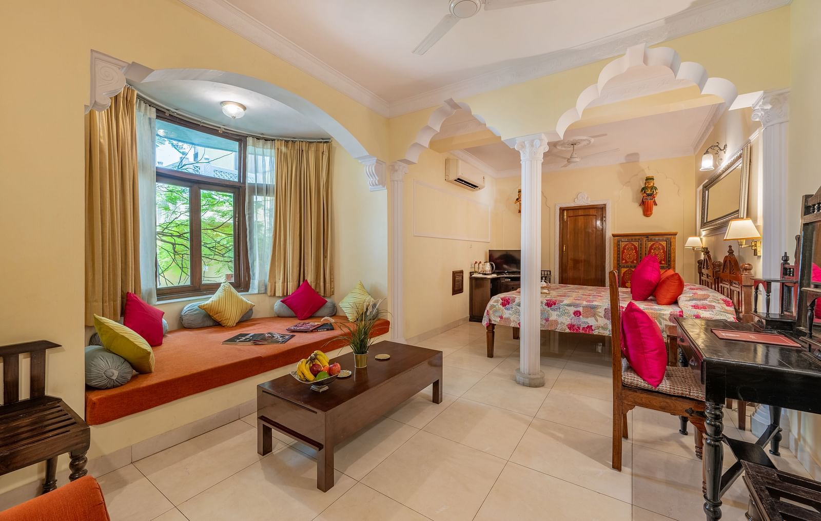 A room with a window seat, colourful cushions, a coffee table, and arched architectural details | Dera Rawatsar, Jaipur