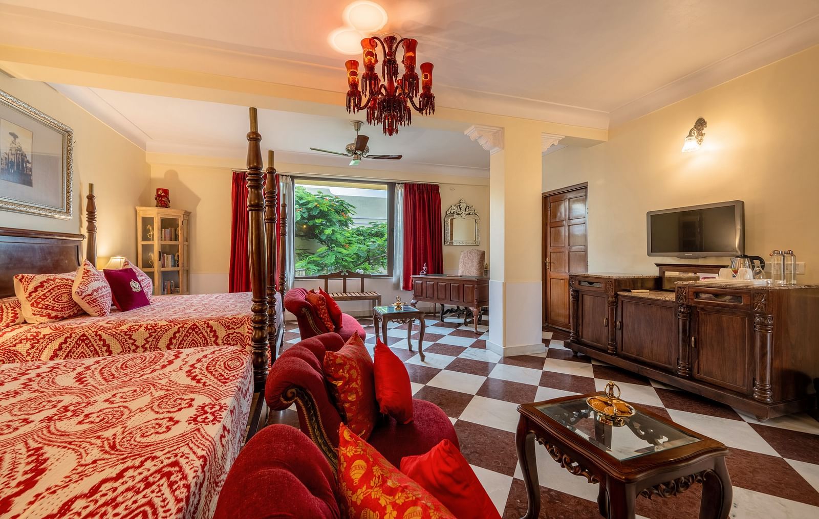 A luxurious suite at Dera Rawatsar, Jaipur, offers two elegant beds, a comfortable seating area, a television, and striking checkered flooring.