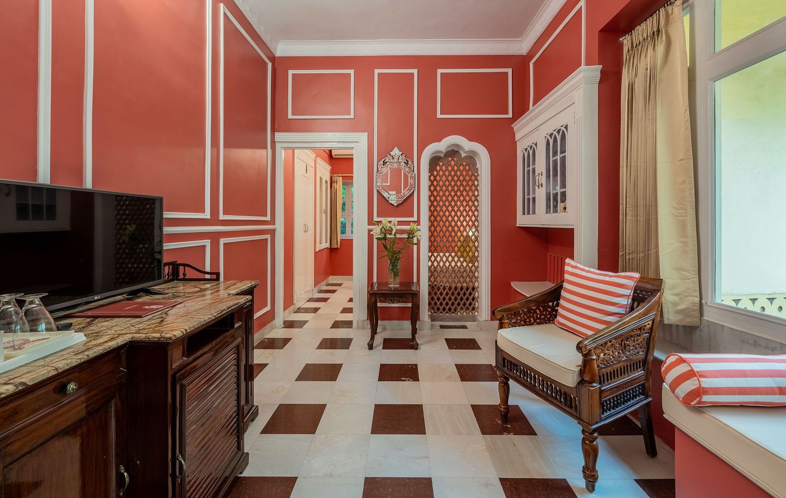 A room with red walls, white trim, a checkered floor, a wooden chair with a striped cushion, and a television | Dera Rawatsar, Jaipur