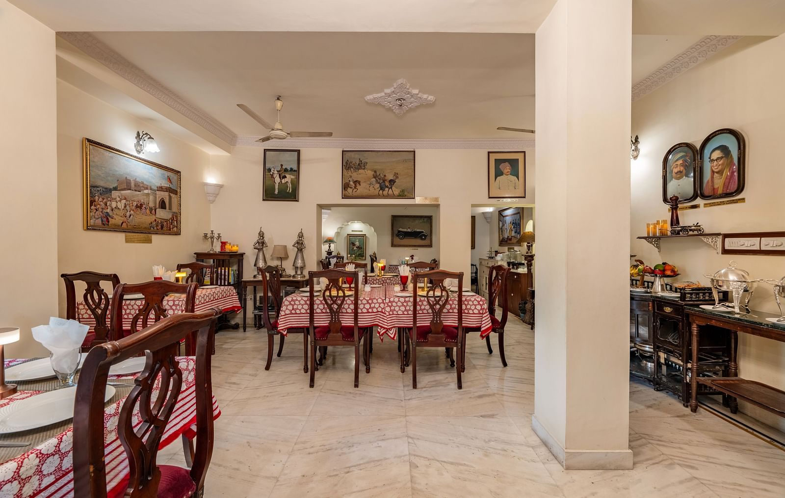The inviting dining space at Dera Rawatsar, Jaipur, features multiple set tables with patterned cloths, wooden chairs, and an array of framed pictures on the walls.