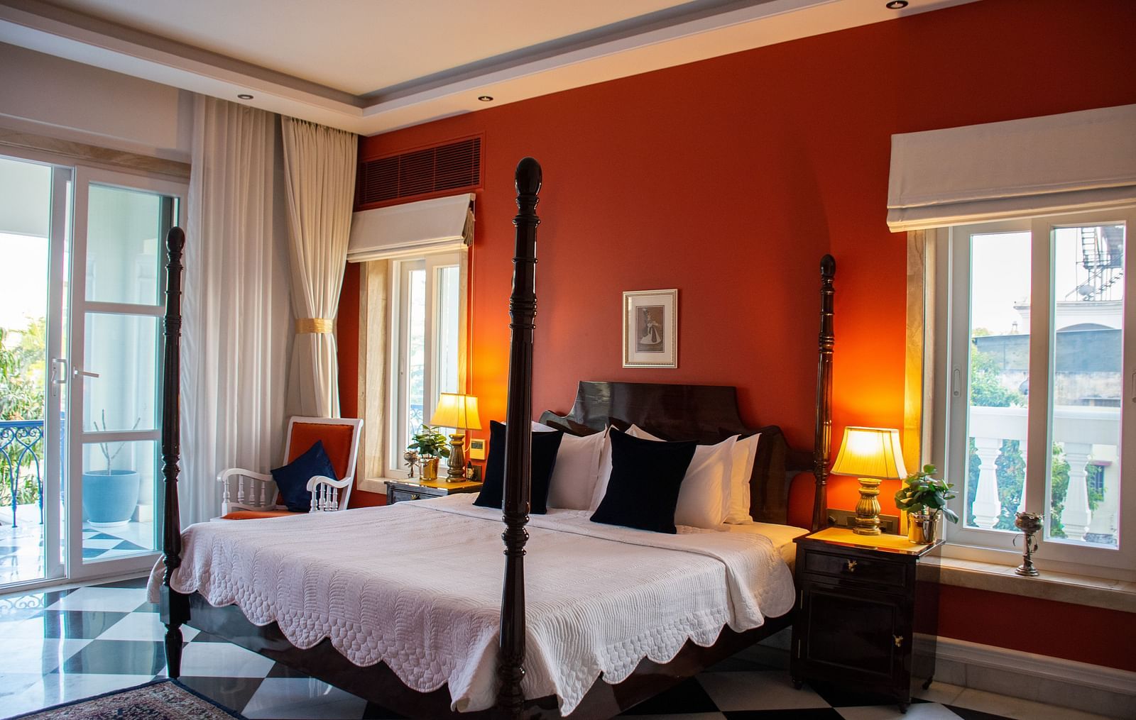 A room at Dileep Kothi, Jaipur with a double bed, side tables with night lamps, French windows and a red wall behind the bed