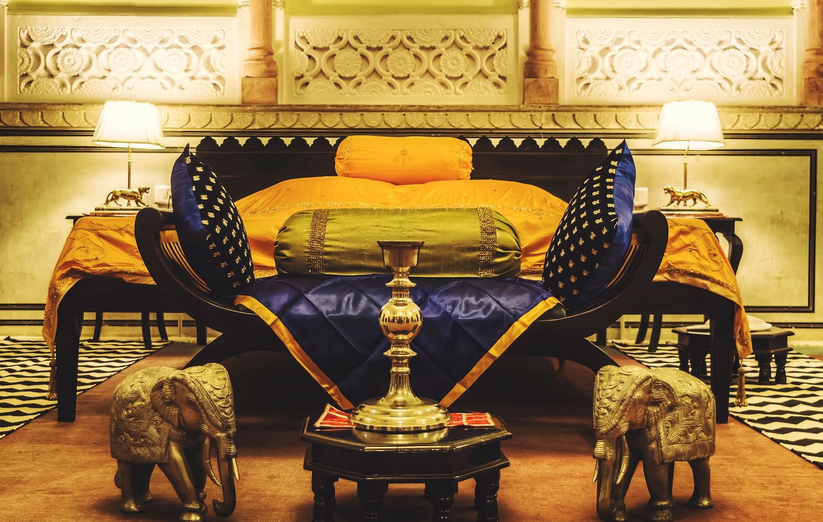 A luxuriously decorated bed at Umaid Vilas Jaipur with ornate elephant sculptures at its foot, showcasing traditional Indian design.