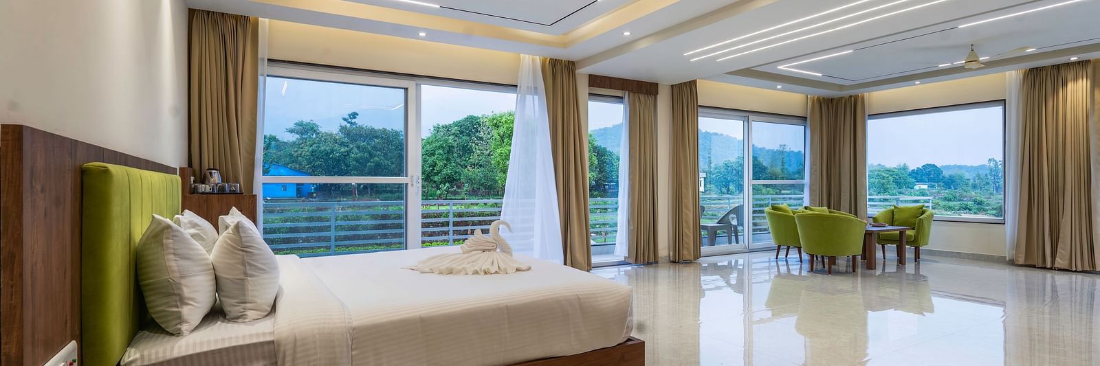 a king size bed beside the floor to ceiling windows in the suite at Corbett Four Seasons, Ramnagar