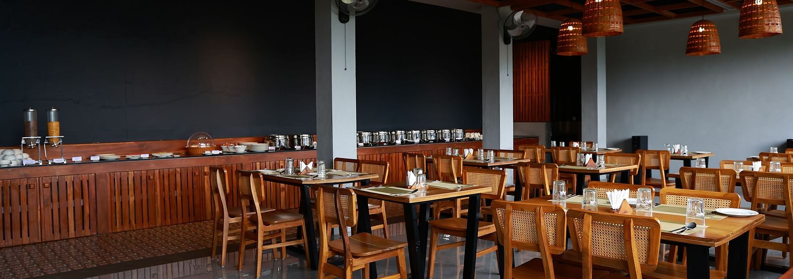  A well-appointed dining area at Vaastha Vagamon, featuring numerous tables and chairs, a buffet spread, and modern lighting fixtures.