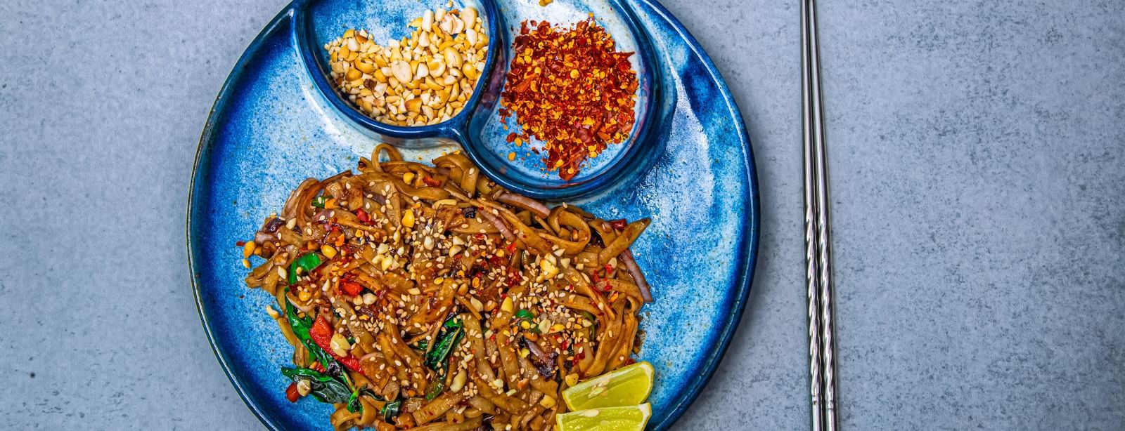 A blue plate with noodles garnished with herbs and served with crushed peanuts and chili flakes in small side compartments at The Hamuse Hotel, Kodaikanal.