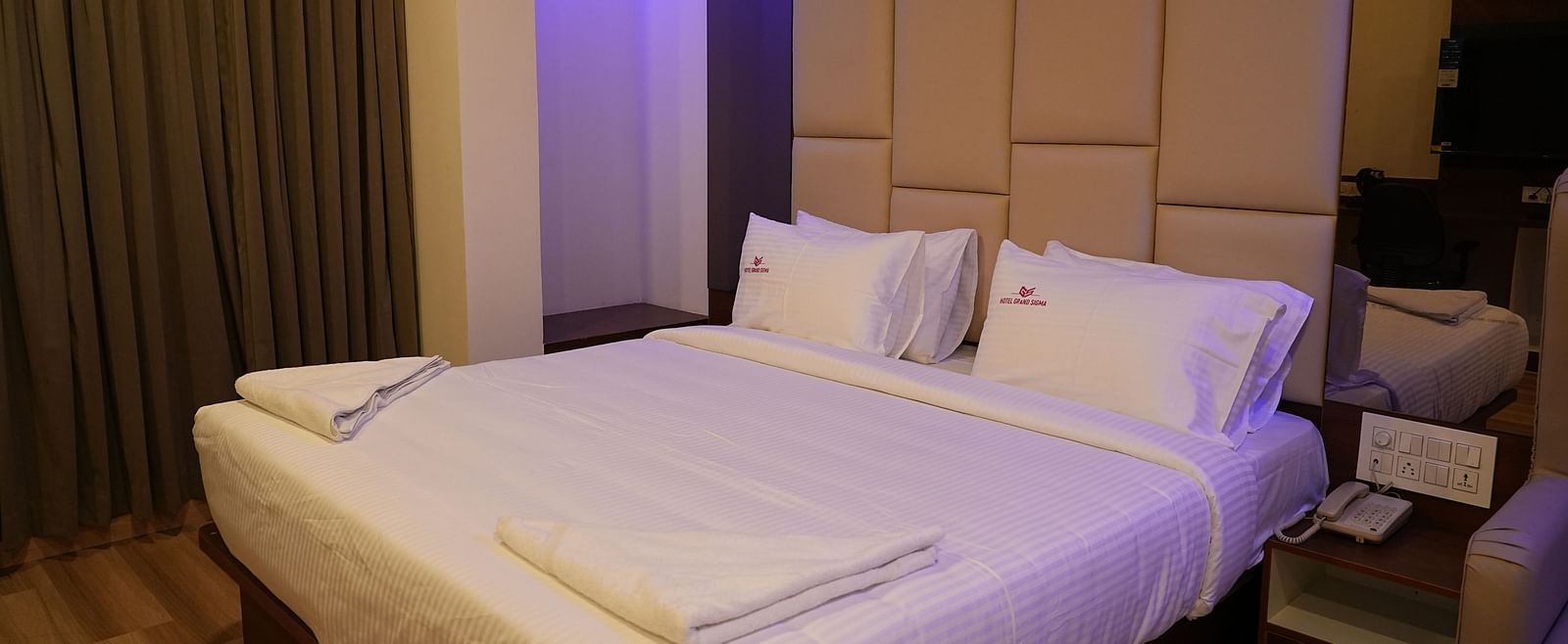 corner view of the double bed of the suite with cushioned headboard behind the bed and close curtains in the corner of the room - Hotel Grand Sigma