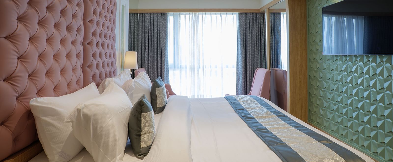 A modern hotel room features a bed with white linens and a television mounted on the wall - Melior Inn