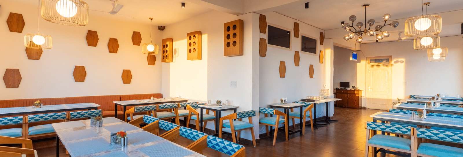 A bright dining room featuring wooden tables, blue chairs, and stylish honeycomb wall decorations at Himalayas Resort By The Lake Hill, Mukteshwar.