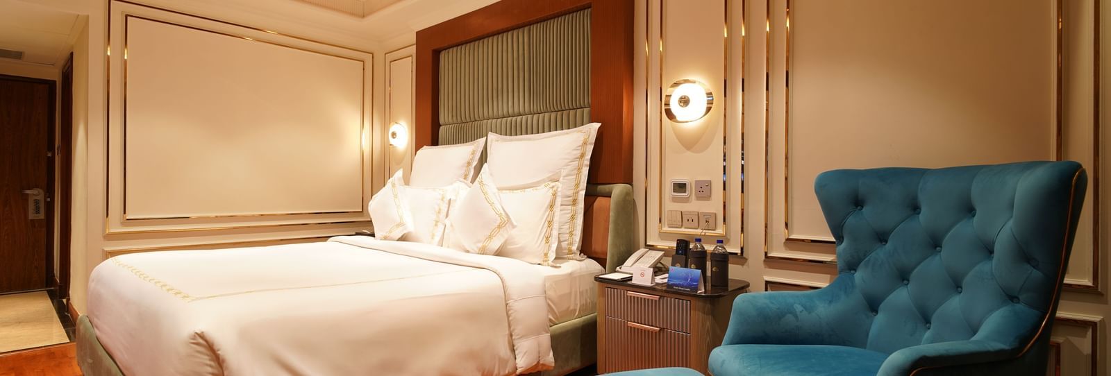 King-size bedroom with teal armchair, side table, and elegant panelling at Accord Metropolitan.