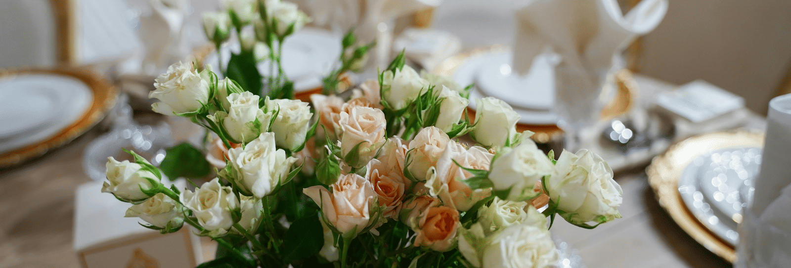 A close up shot of a beautiful flower vase with a lot of white and pink roses on a dining table.