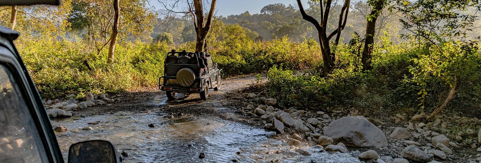 Two safari jeeps traversing through a stony water stream in Jim Corbett.